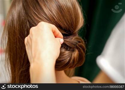 Hands of hairdresser making french twist hairstyle of an unrecognizable young brunette woman in a beauty salon, back view, close up. Hands of hairdresser making french twist hairstyle of an unrecognizable young brunette woman in a beauty salon, back view, close up.