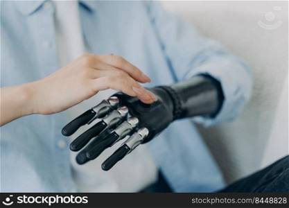 Hands of handicapped girl setting up her bionic arm and pressing buttons. Young european woman with cyber hand at home. Modern robotic bionic prosthesis. Futuristic technology and engineering concept.. Hands of handicapped girl setting up her bionic arm and pressing buttons. Robotic bionic prosthesis.