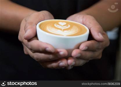 Hands of man holding entwine cup of coffee heart-shaped.