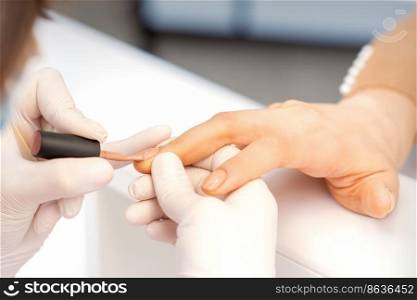Hands of manicure master in white protective gloves apply polish to female fingernails. Hands of manicure master in white protective gloves apply polish to female fingernails.
