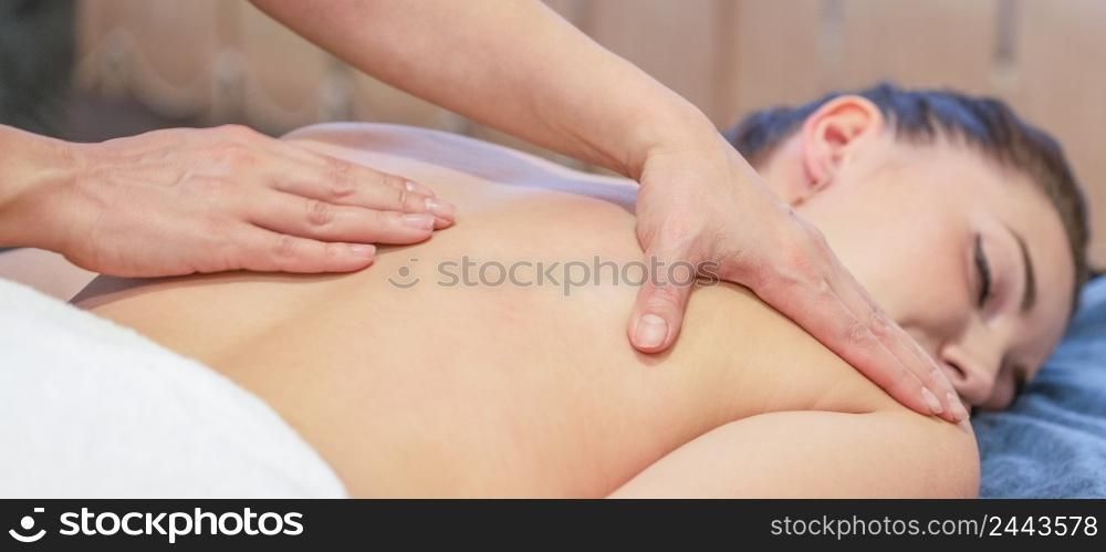 Hands of massage therapist doing massage on back of young girl. Advertising a beauty salon or massage room treatment room. Hands of massage therapist doing massage on back of young girl