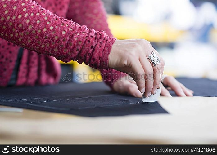 Hands of mature seamstress chalking outline onto textile on work table