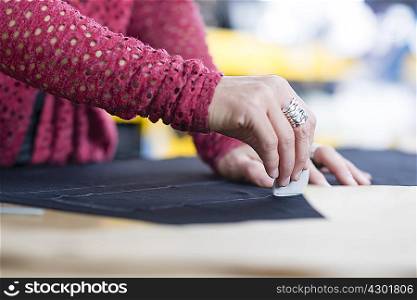 Hands of mature seamstress chalking outline onto textile on work table