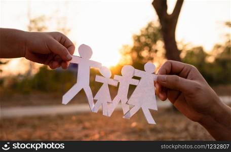 Hands of mother and daughter holding family cut out paper in autumn park on sunset background.