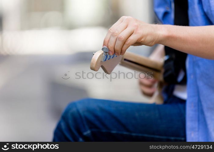 Hands of musician with guitar. Hands of musician tuning his guitar outside