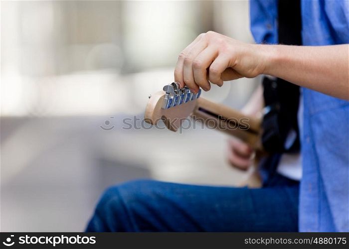 Hands of musician with guitar. Hands of musician tuning his guitar outside