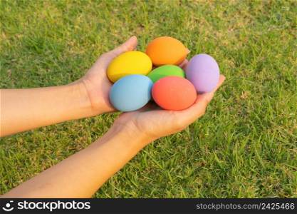Hands of people holding colorful easter eggs on natural green grass background. Food decoration on holiday.