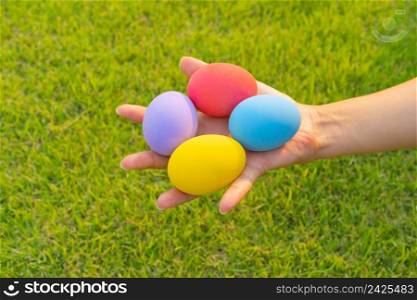 Hands of people holding colorful easter eggs on natural green grass background. Food decoration on holiday.