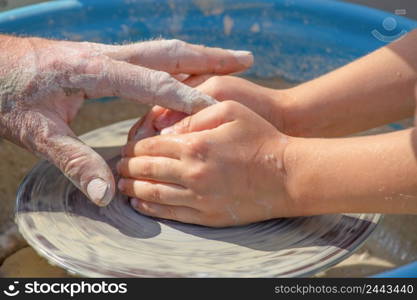 Hands of potter and child work with clay. Potter teaches a child to work with raw clay on a potter&rsquo;s wheel. Hands of potter and child work with clay