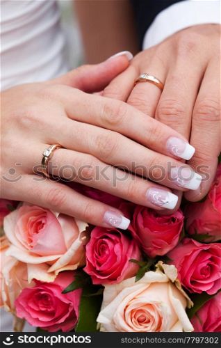 hands of the bride and groom with the rings lying on the bouquet