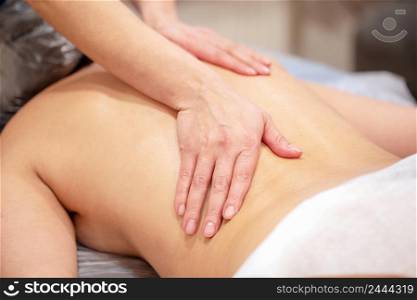 Hands of the masseur on back of young woman. Selective focus on the main subject. Hands of the masseur on back of young woman