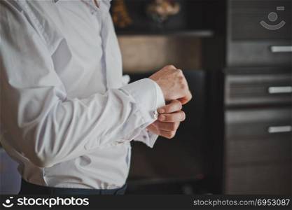 Hands of the young man clasping cuff links on shirt cuffs.