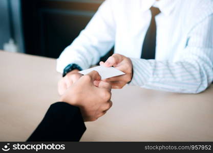 Hands of two business people sitting in office room giving and taking empty business card.