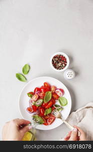 Hands of woman cooking fresh salad (tomato, basil, onion, olive oil) on rustic background. Top view