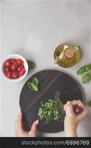 Hands of woman cooking italian food (tomato, basil, olive oil) on rustic background. Top view