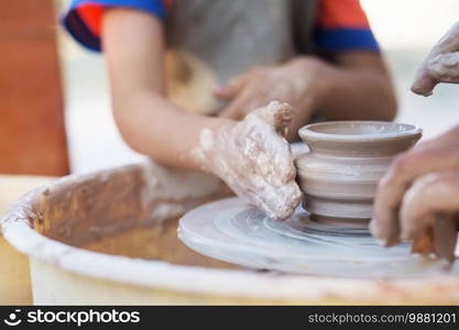 Hands of young potter, creating an earthen jar on the circle, close-up