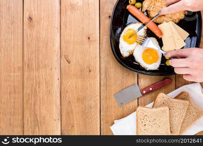 Hands over breakfast plate. Fried egg, wholegrain toast, cheese, hotdog and cup of coffee for breakfast over wooden table, top view, copy space