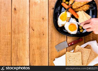 Hands over breakfast plate. Fried egg, wholegrain toast, cheese, hotdog and cup of coffee for breakfast over wooden table, top view, copy space