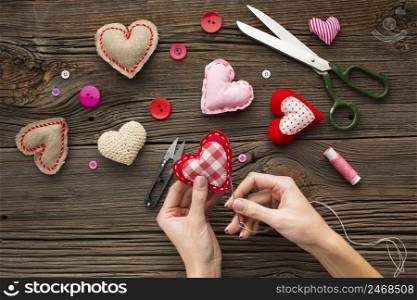 hands sewing red heart shape wooden background