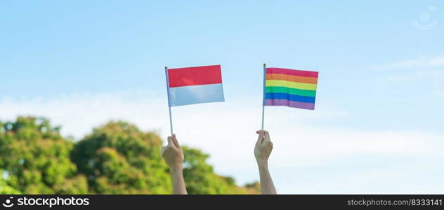 hands showing LGBTQ Rainbow and Indo≠sia flag on nature background. Support Lesbian, Gay, Bisexual, Trans≥nder and Queer comμnity and Pride month concept