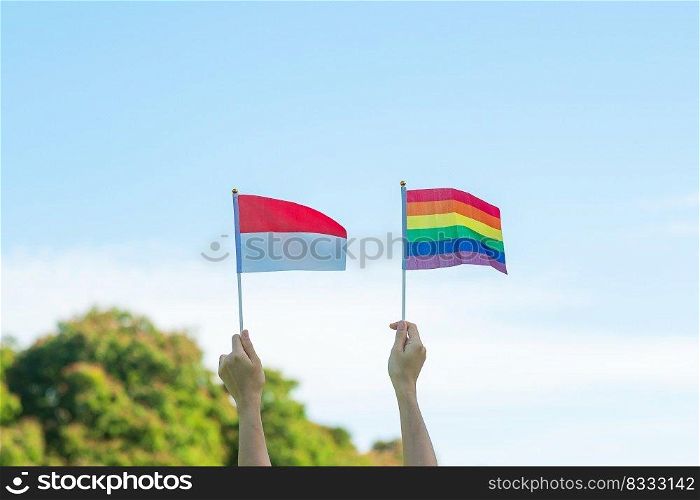hands showing LGBTQ Rainbow and Indonesia flag on nature background. Support Lesbian, Gay, Bisexual, Transgender and Queer community and Pride month concept