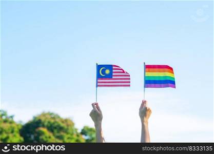 hands showing LGBTQ Rainbow and Malaysia flag on nature background. Support Lesbian, Gay, Bisexual, Transgender and Queer community and Pride month concept