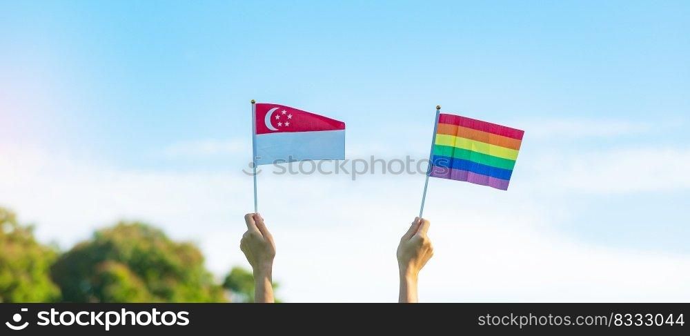 hands showing LGBTQ Rainbow and Singapore flag on nature background. Support Lesbian, Gay, Bisexual, Transgender and Queer community and Pride month concept