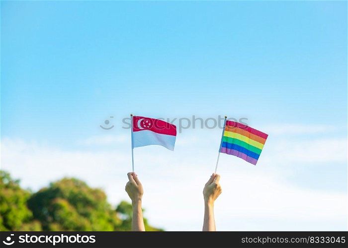 hands showing LGBTQ Rainbow and Singapore flag on nature background. Support Lesbian, Gay, Bisexual, Transgender and Queer community and Pride month concept