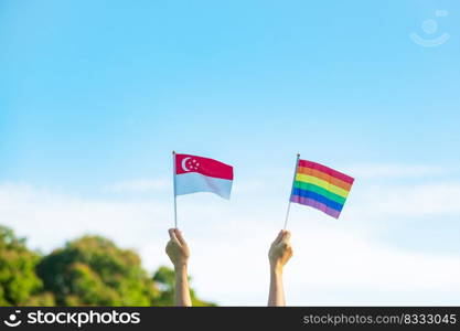 hands showing LGBTQ Rainbow and Singapore flag on nature background. Support Lesbian, Gay, Bisexual, Transgender and Queer community and Pride month concept