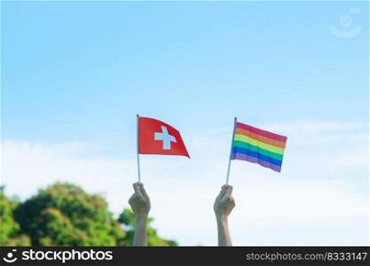 hands showing LGBTQ Rainbow and Switzerland flag on nature background. Support Lesbian, Gay, Bisexual, Transgender and Queer community and Pride month concept