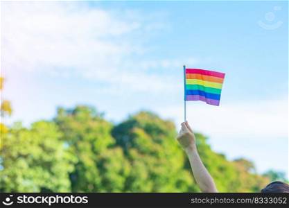 hands showing LGBTQ Rainbow flag on nature background. Support Lesbian, Gay, Bisexual, Transgender and Queer community and Pride month concept