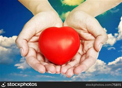 Hands showing red heart on sky background