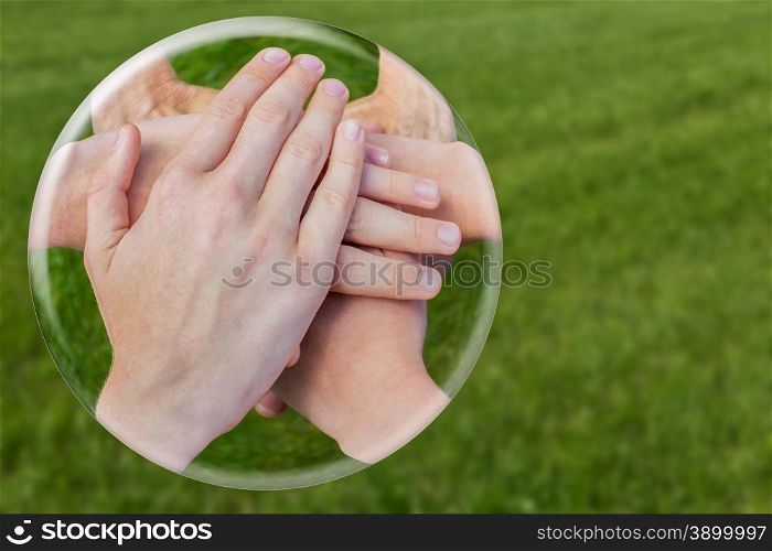 Hands uniting joining in glass ball isolated on green grass
