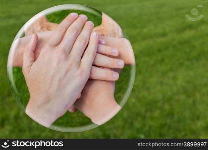 Hands uniting joining in glass ball isolated on green grass
