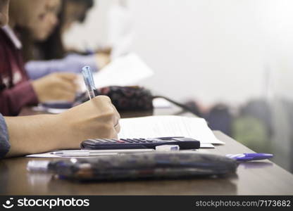 Hands university student holding pen writing /calculator doing examination / study or quiz, test from teacher or in large lecture room, students in uniform attending exam classroom educational school.