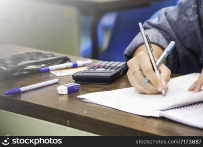 Hands university student holding pen writing /calculator doing examination / study or quiz, test from teacher or in large lecture room, students in uniform attending exam classroom educational school.