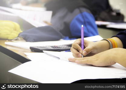 Hands university student holding pen writing /calculator doing examination / study or quiz, test from teacher or in large lecture room, students in uniform attending exam classroom educational school.