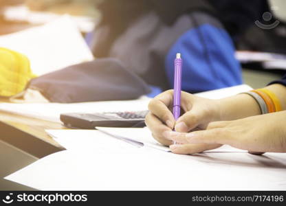 Hands university student holding pen writing /calculator doing examination / study or quiz, test from teacher or in large lecture room, students in uniform attending exam classroom educational school.