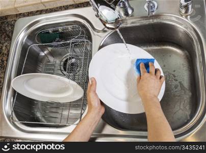 Hands washing dishes with running water from faucet in sink