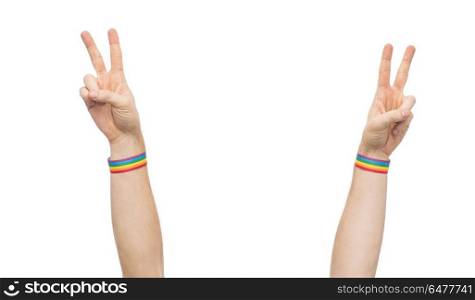 hands with gay pride rainbow wristbands make peace. lgbt, same-sex relationships and homosexual concept - close up of male hands wearing gay pride awareness wristbands showing peace sign