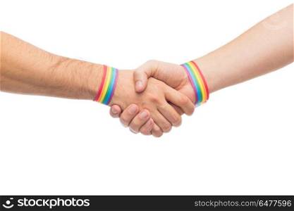 hands with gay pride wristbands make handshake. lgbt, same-sex love and homosexual relationships concept - close up of male couple hands with gay pride rainbow awareness wristbands making handshake