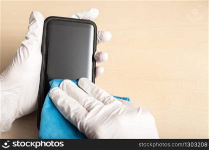 Hands with gloves cleaning mobile phone with disinfectant. COVID-19 Coronavirus prevention concept. Copy space