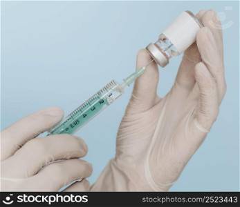 hands with gloves holding vaccine bottle with syringe