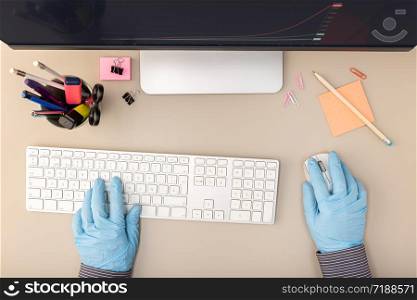 Hands with protective glove typing on keyboard computer. Worker taking precautions during the coronavirus COVID-10 outbreak. Top view