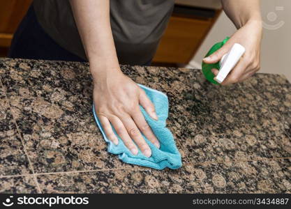 Hands with rag and spray bottle cleaning stone counter-top