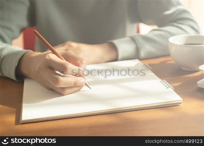 hands woman writing notebook. On wooden desk background have coffee cup and laptop in morning light.