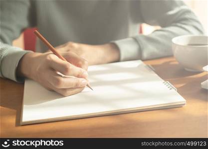hands woman writing notebook. On wooden desk background have coffee cup and laptop in morning light.