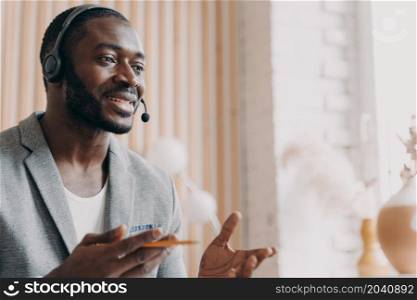 Handsome african american businessman in headset speaking by video call in office, dark-skinned business ptoffesional consulting client online while sitting at his workplace. Handsome african american businessman in headset speaking by video call in office