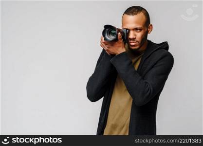 Handsome african american guy holding digital camera over light gray background.. Handsome african american guy holding digital camera over light gray background