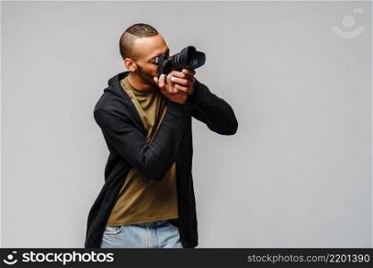 Handsome african american guy holding digital camera over light gray background.. Handsome african american guy holding digital camera over light gray background